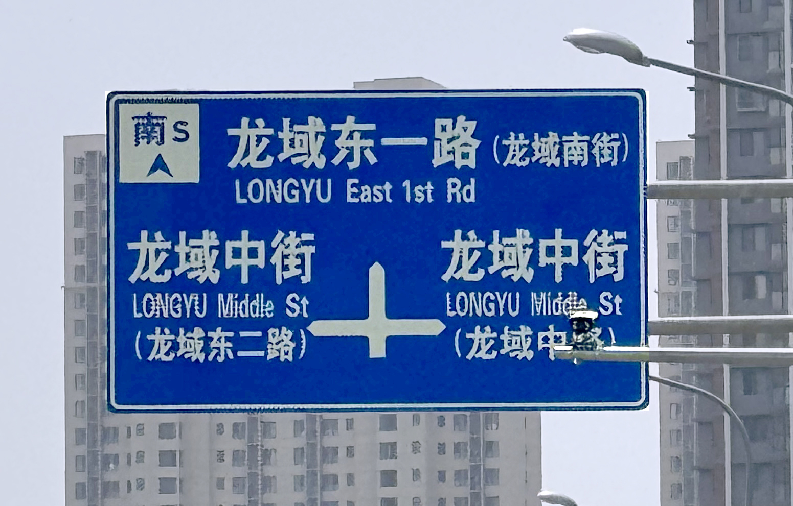 A streetsign for an intersection. If you are Chinese, you might be able to read the sign and attain a sense of place. Otherwise and regardless, the sign is likely to be familiar, as there are apparently standards of some sort for street (or highway) signage.